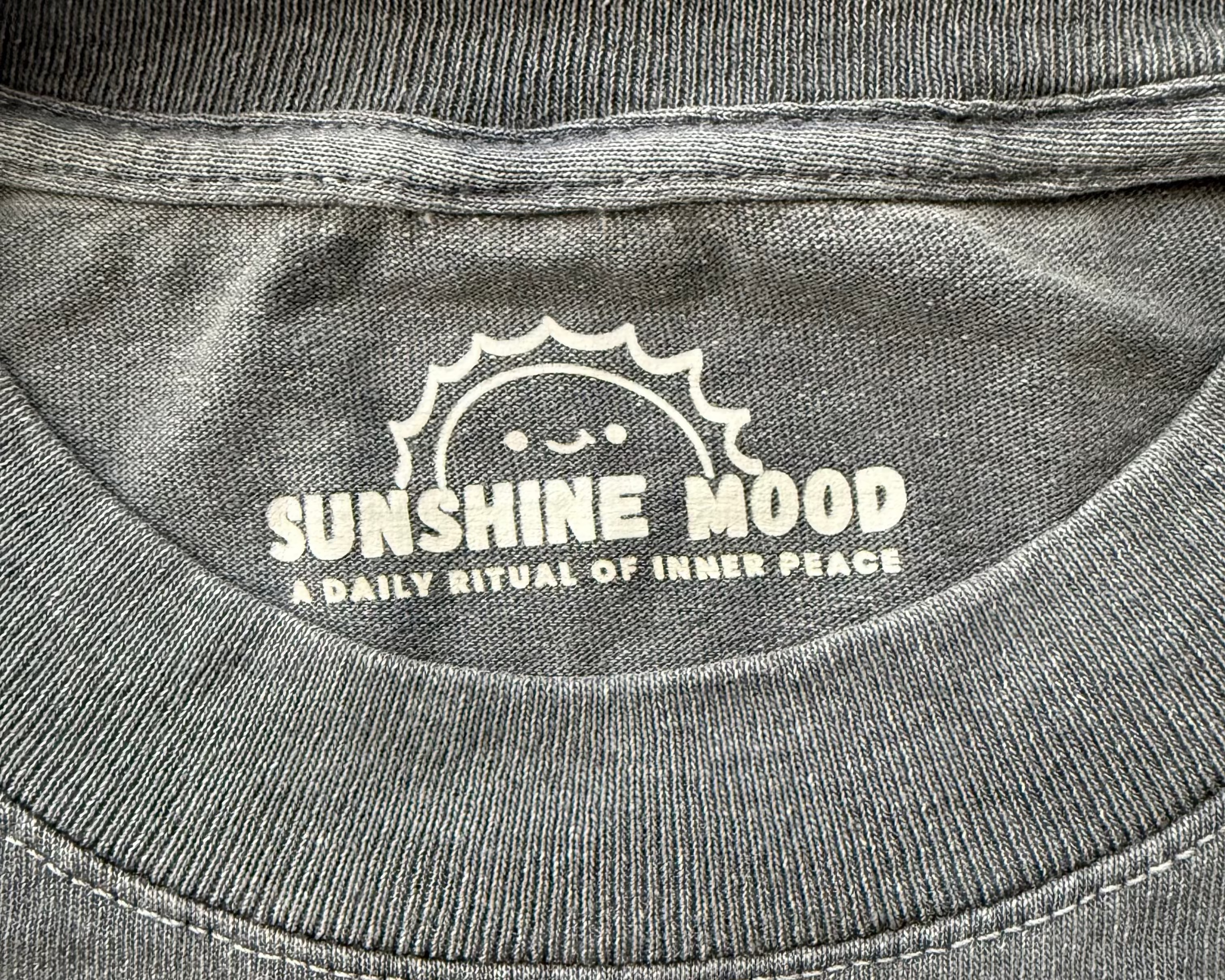 Close-up of Sunshine Mood Faded Black tee inner neck print with smiling sun logo and “A Daily Ritual of Inner Peace.”