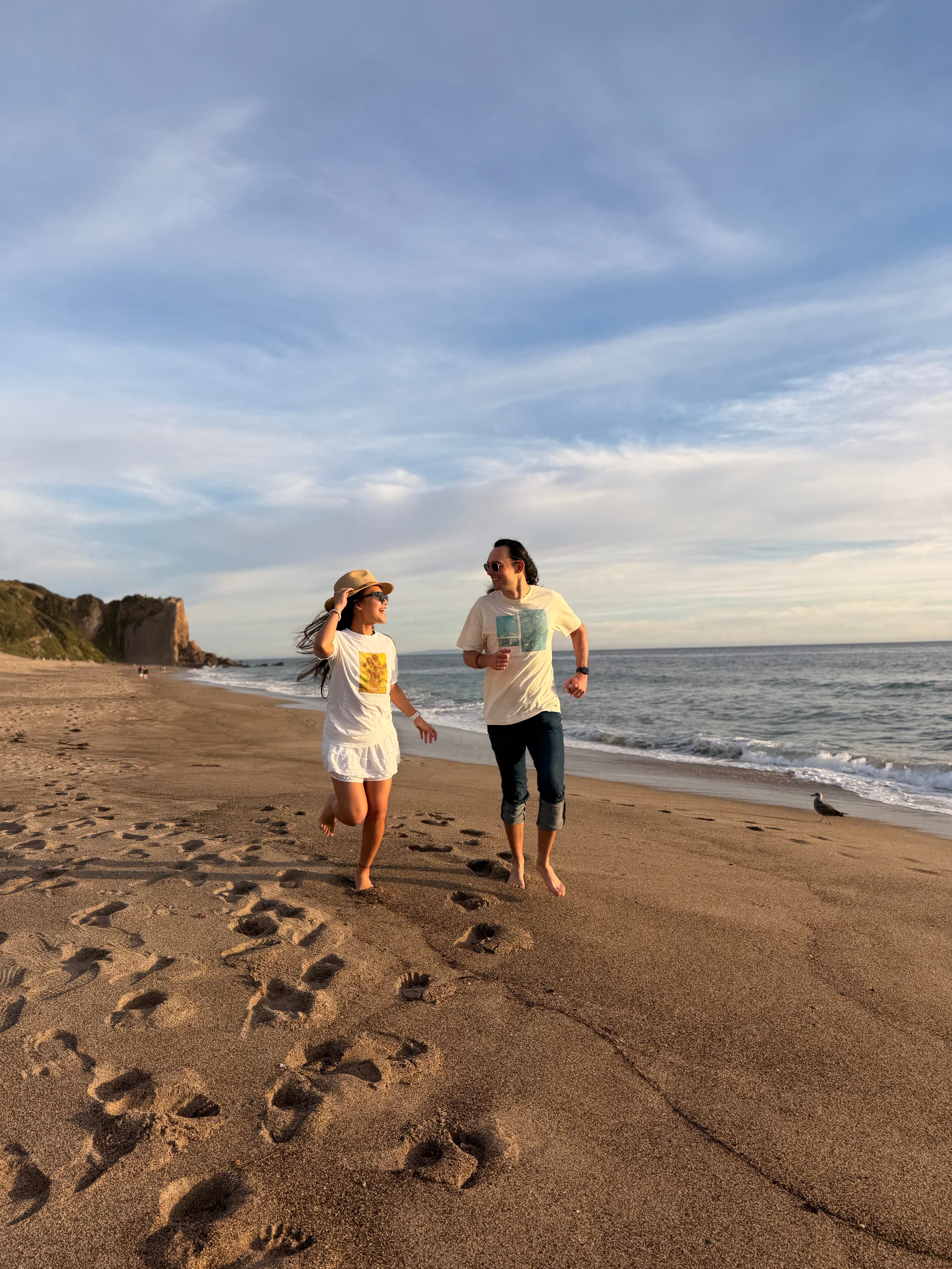 Sunshine Mood tees worn by two models on a twilight beach featuring relaxed silhouettes and fine art graphics